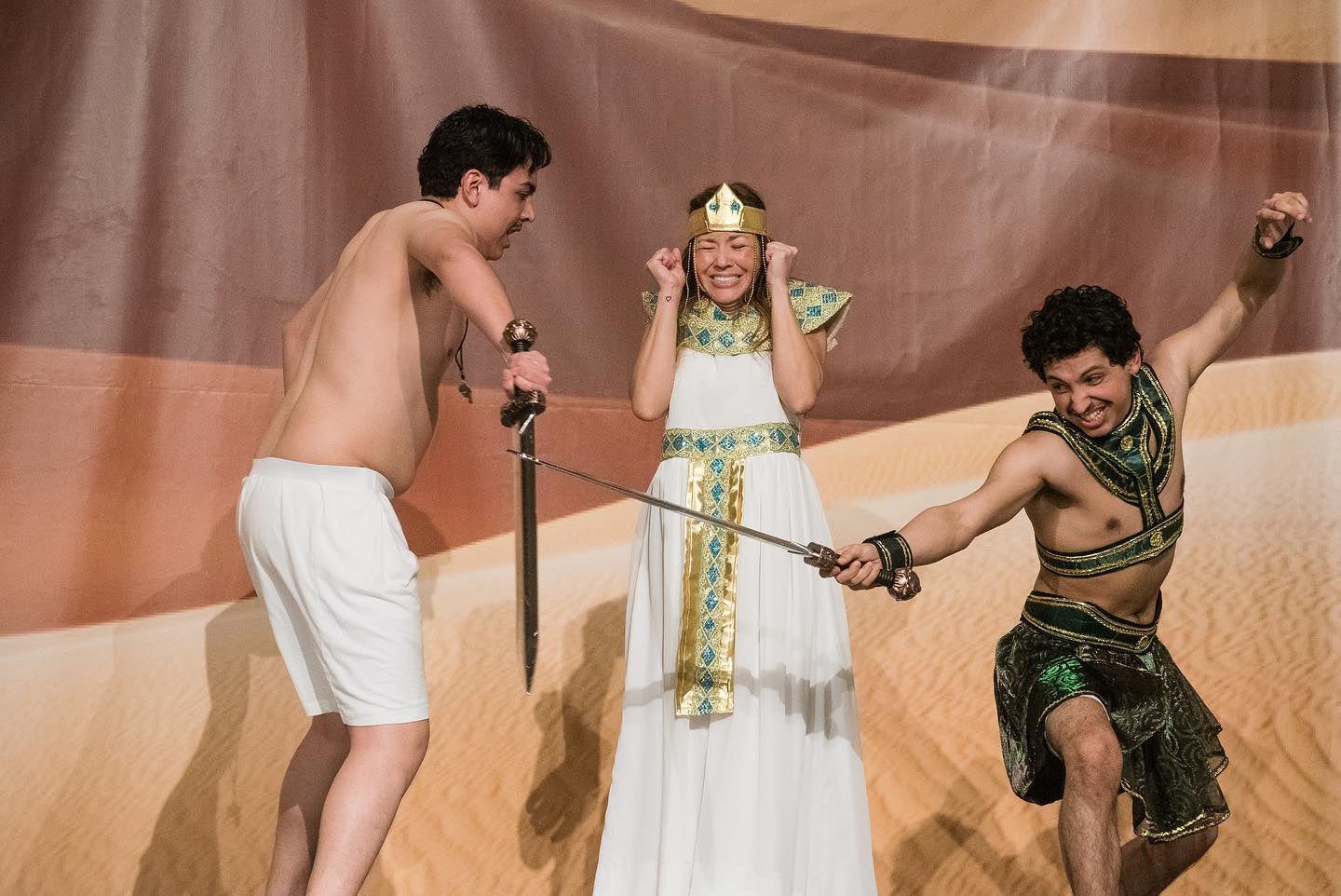 An egyptian monarch is showing frustration as a person (presumably a slave) is lashing out at another man in front. These are all actors.