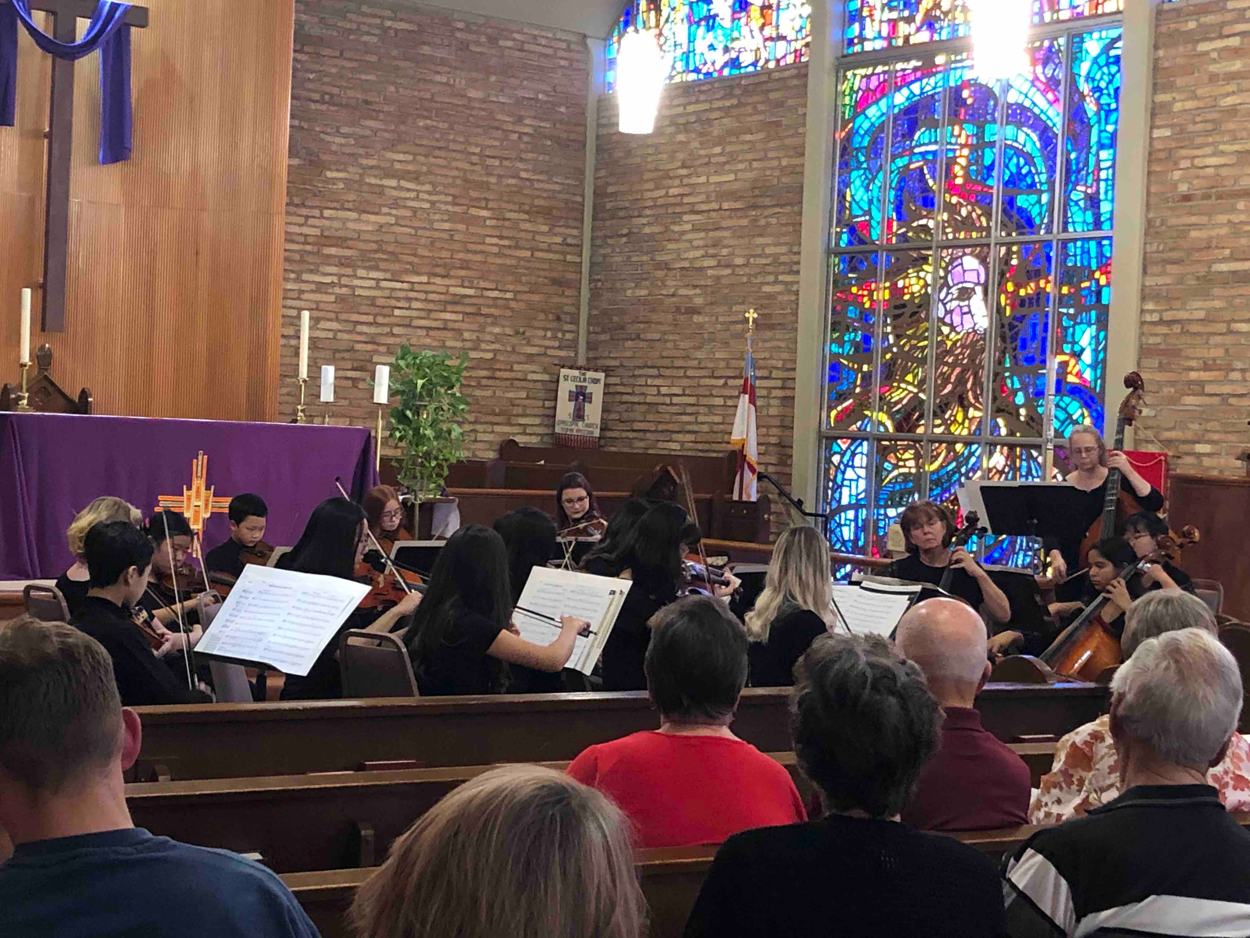 Audience members sit in the rows of a large church with stained-glass windows.