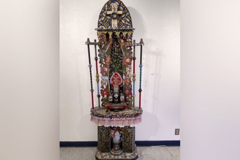 A window-like altar is decorated with many dim colors, flowers, and a cross