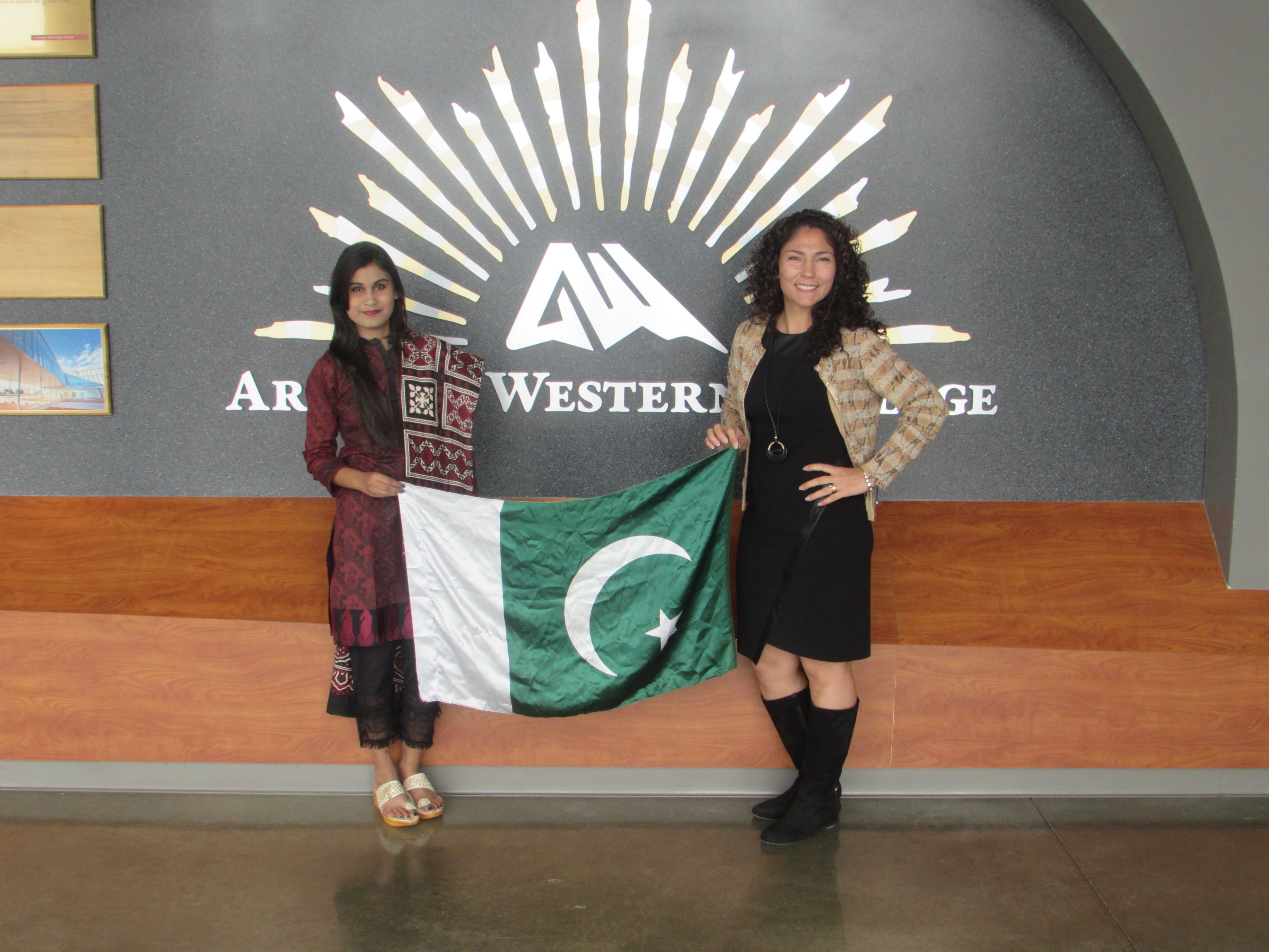 Two women hold up a Pakistani flag. one is wearing traditional Pakistani dress.