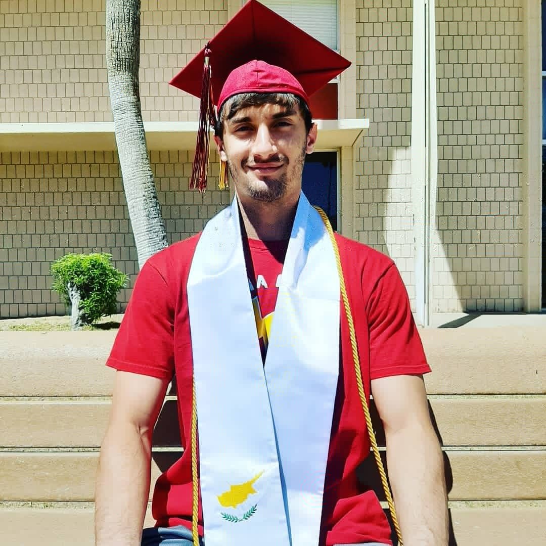 A graduate stands wearing sashes and a cap in front of AWC building AC