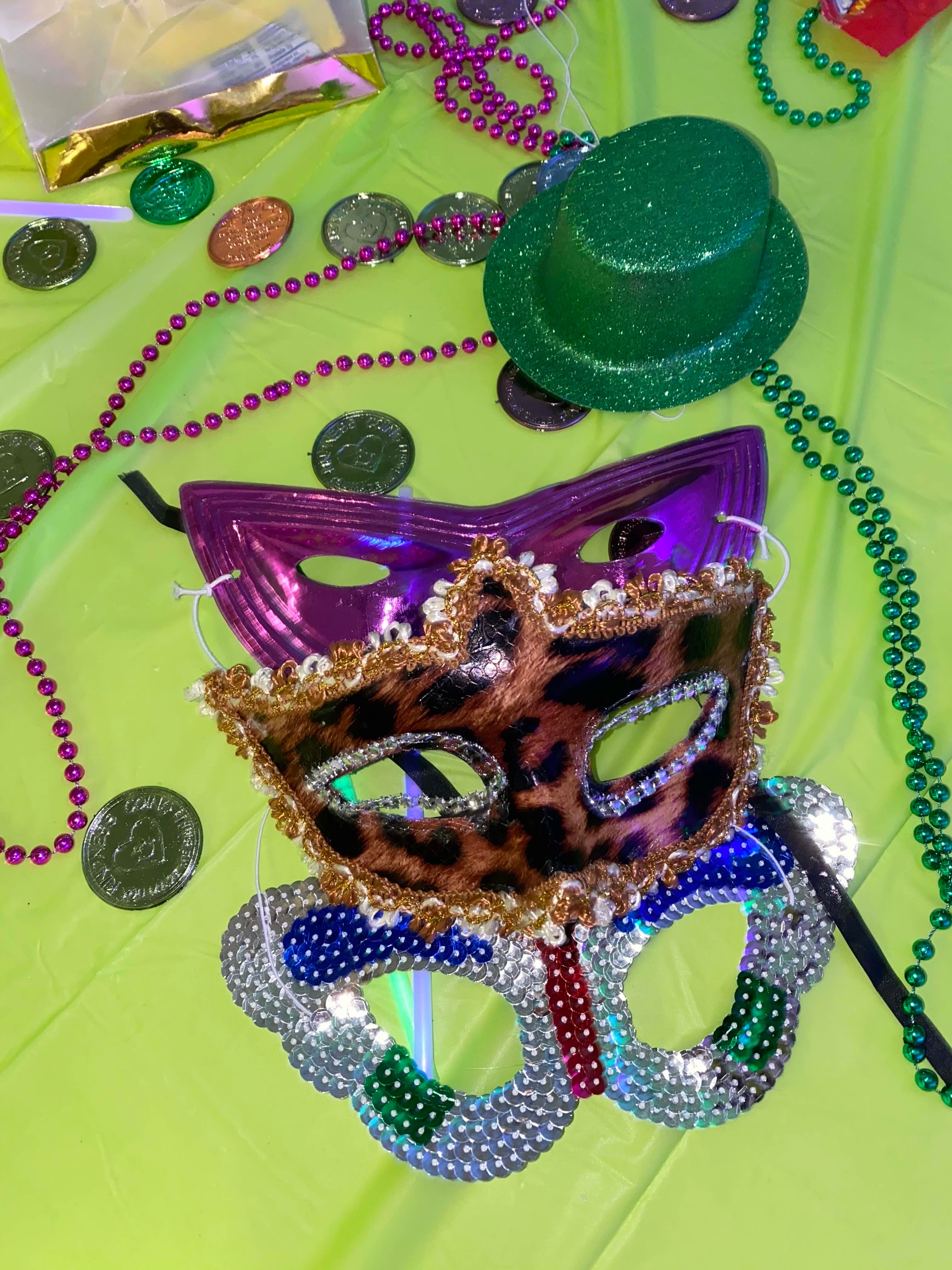 mardi gras masks, beads, coins, and a hat are strewn on a green table