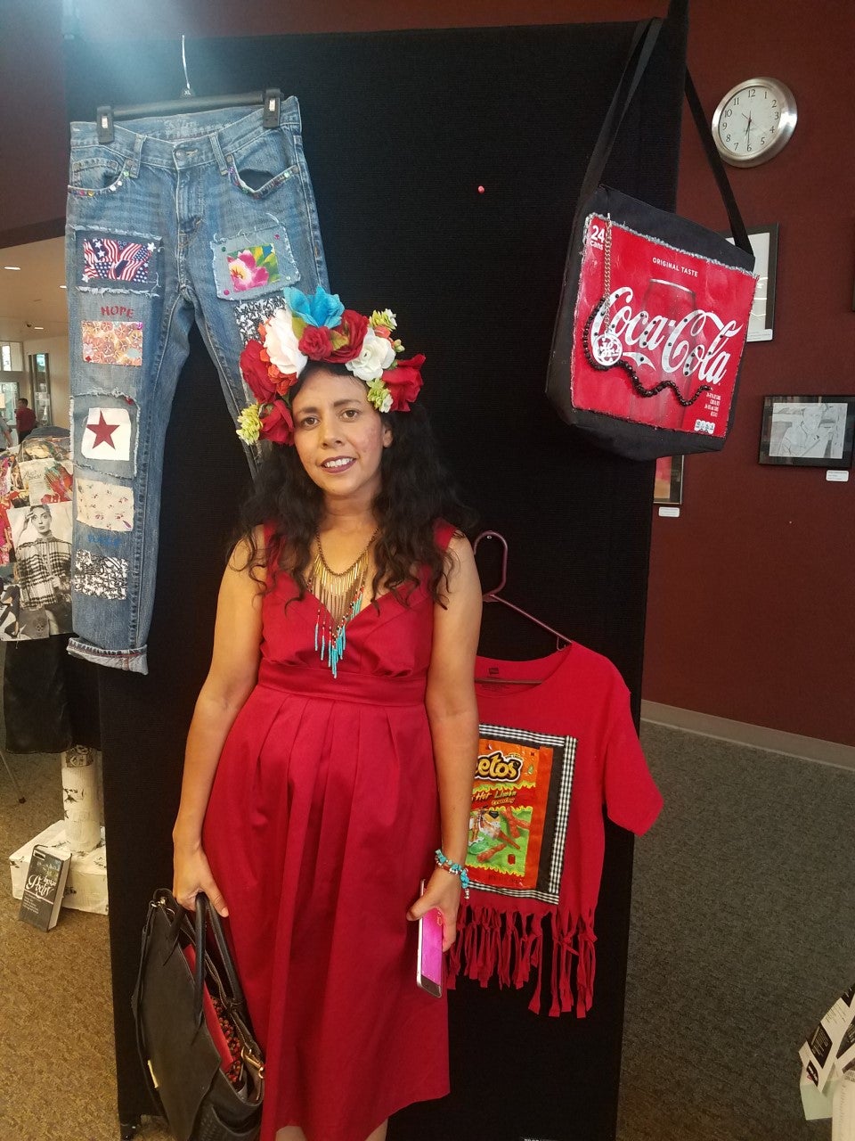 A woman in a red dress and flower crown standing beside mixed media art/clothing