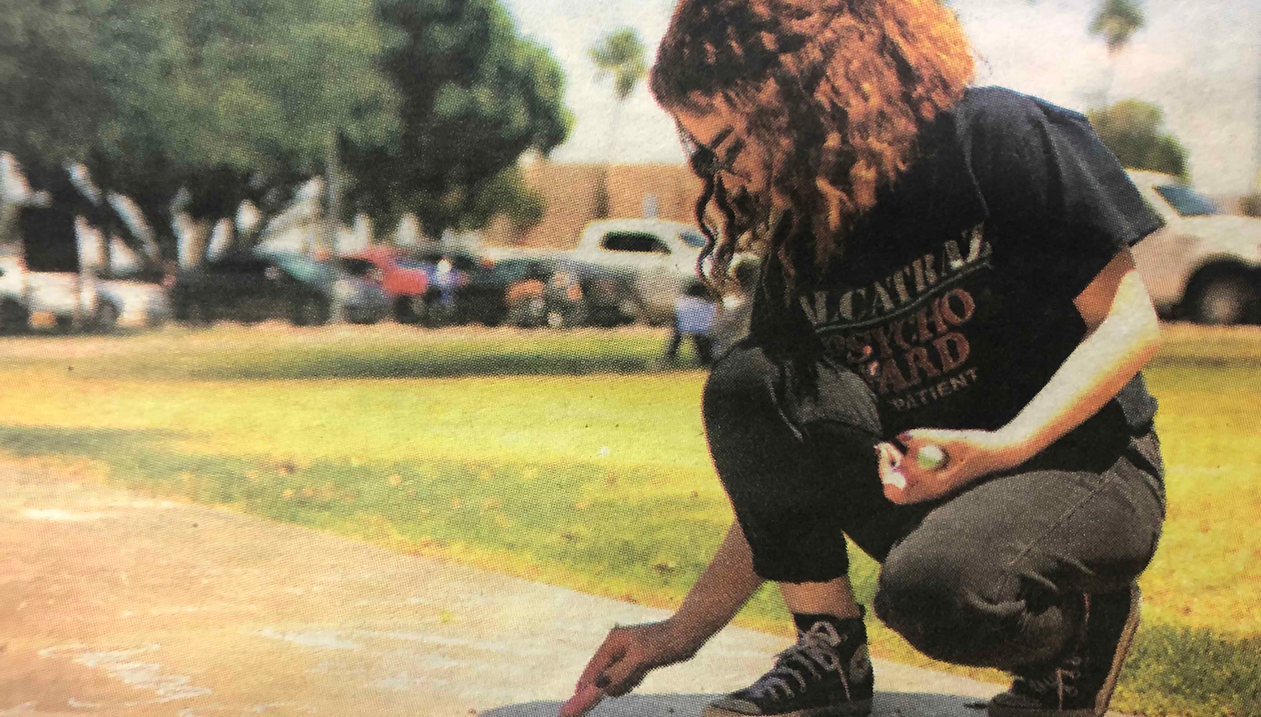 An AWC student writes "gregueria" on campus sidewalk at the Student Art Exhibit Reception in May. Photo Courtesy of AWC Photo Services. Student kneels down to write with chalk on school sidewalk