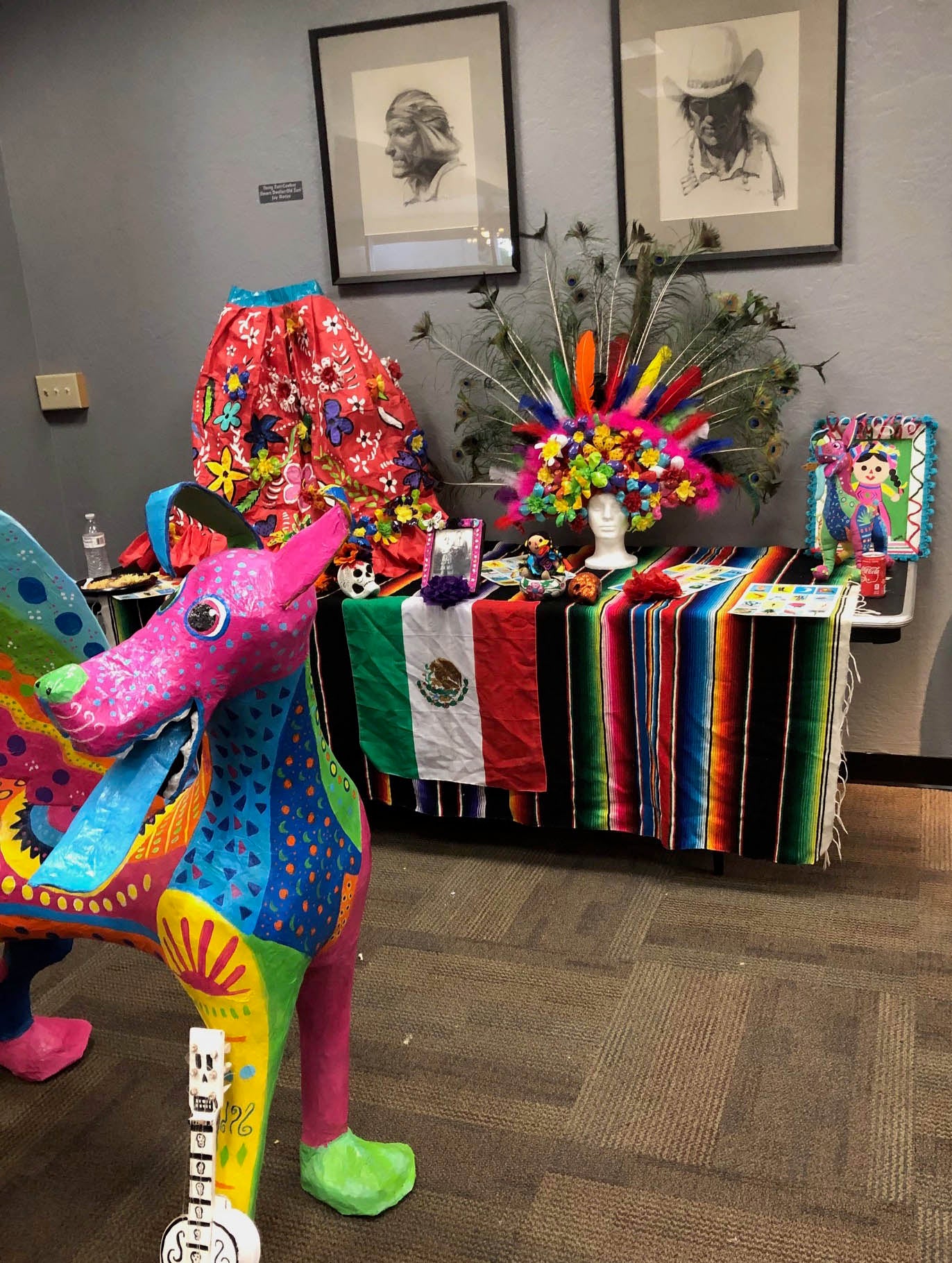 Colorful dog-like sculpture in front of a Mexican heritage display.