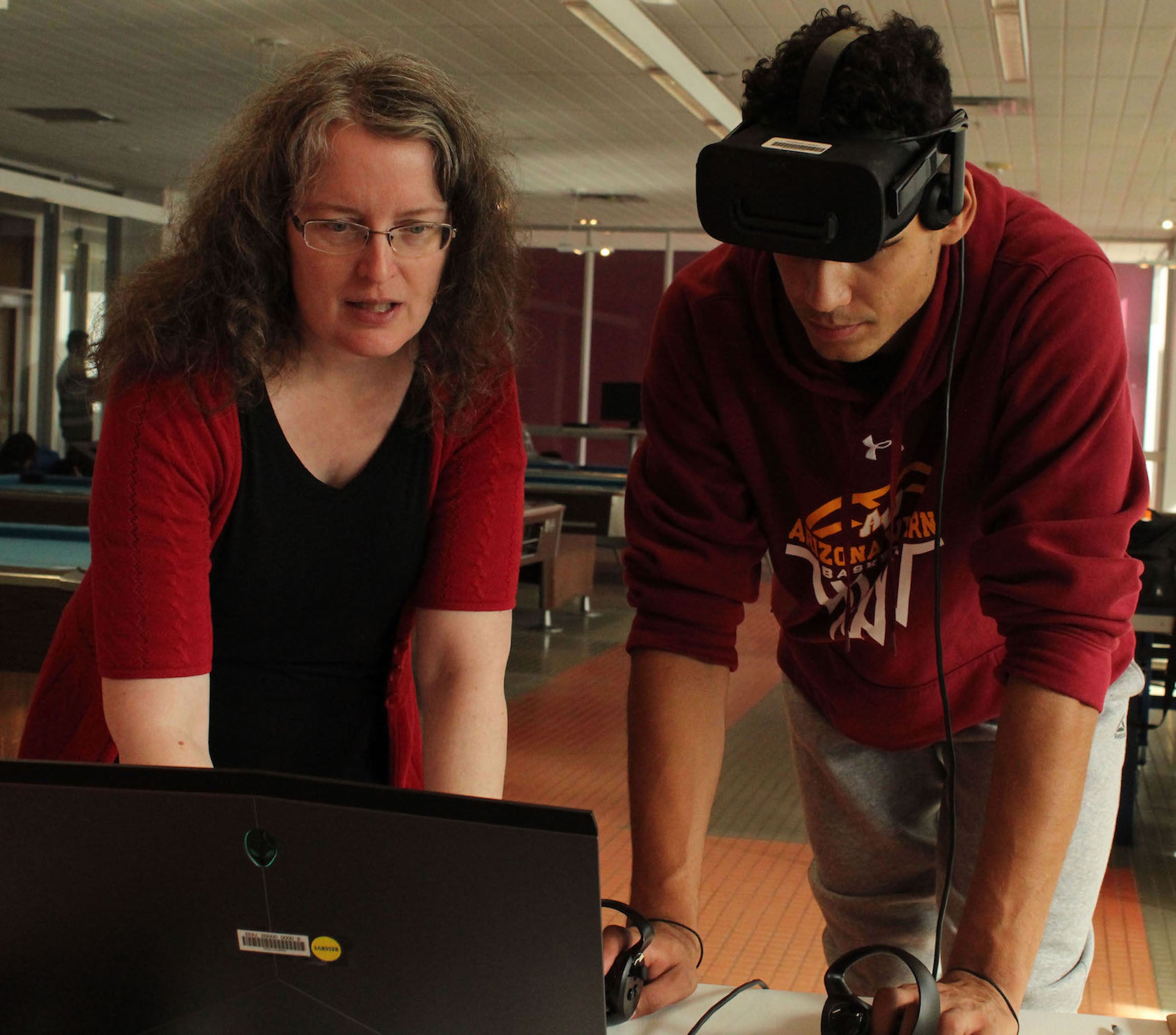 AWC Librarian Wendy Hoag shows a student how to use the new virtual reality technology at the Extra Life charity event. Photo by Zachary Figueroa Two people looking at a computer as if they were setting it up