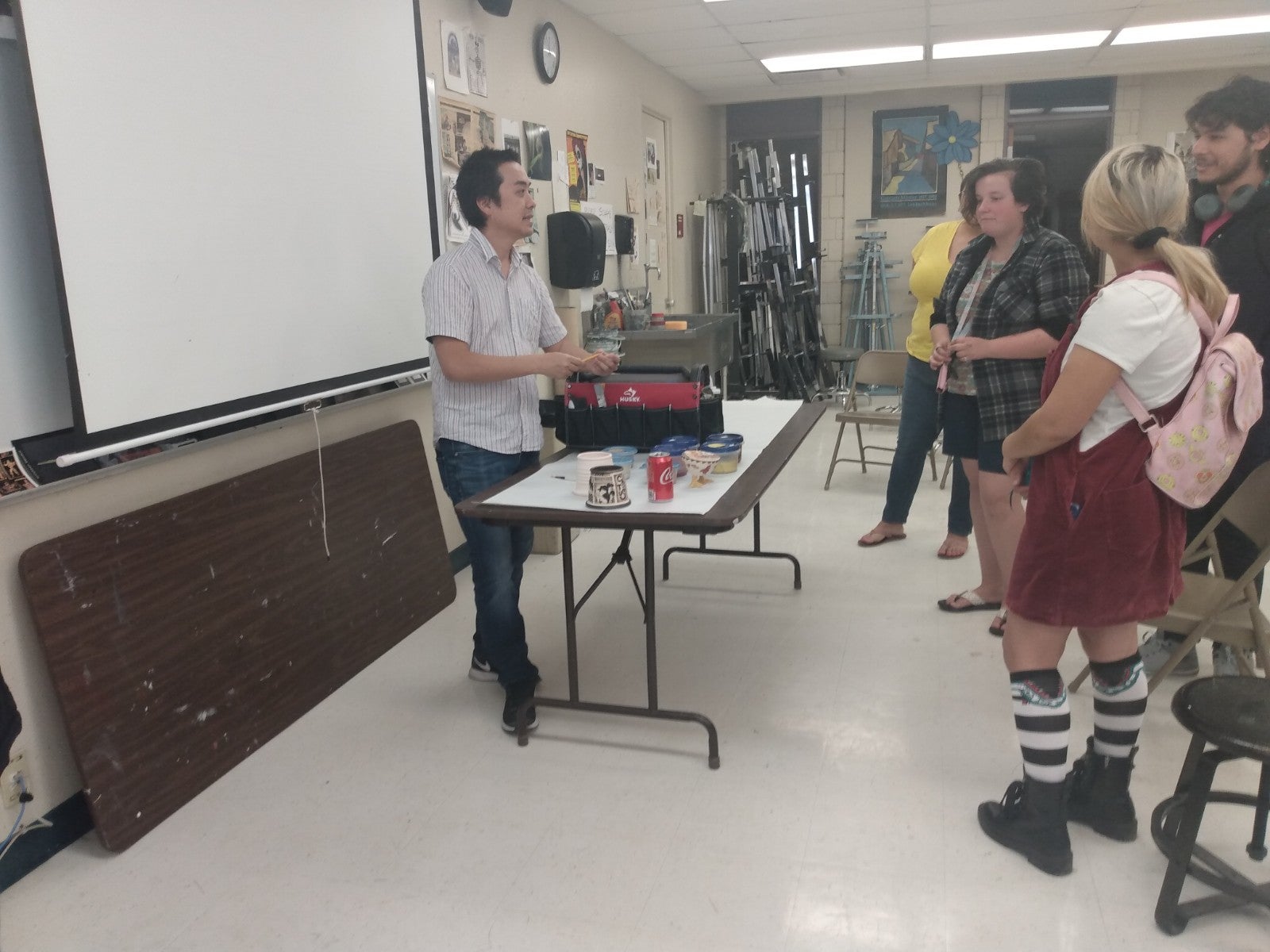 people are standing as a man at a table presents his art