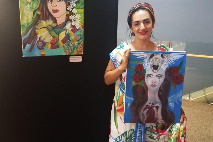A woman dressed like Frida Kahlo holding up a painting by another painting.