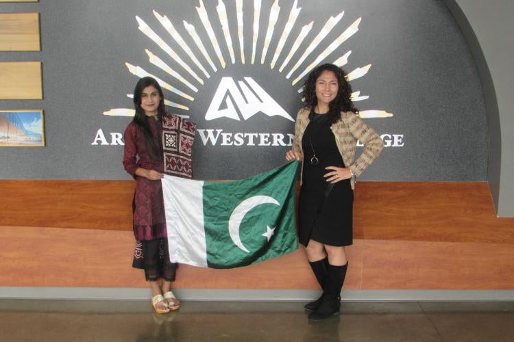 Two women hold up a Pakistani flag. one is wearing traditional Pakistani dress.