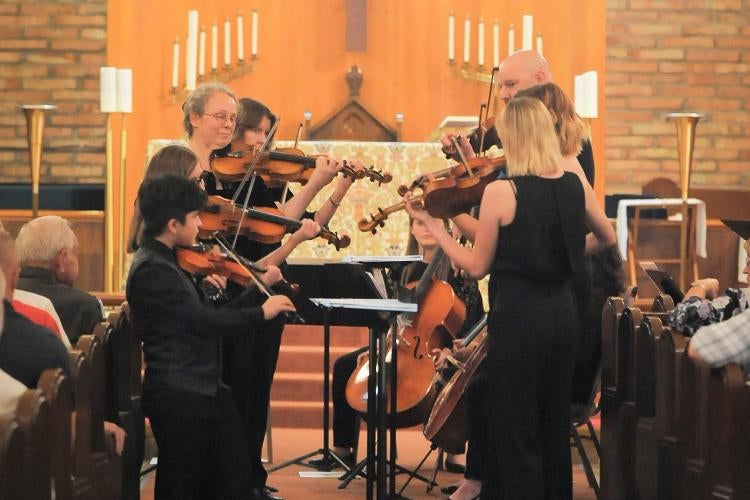 Performers stand playing string instruments in a church