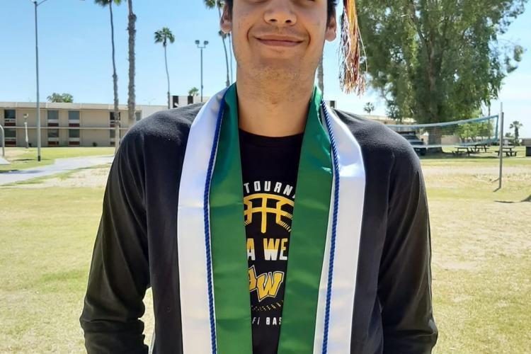 A graduate stands wearing sashes and a cap in front of the AWC dorms