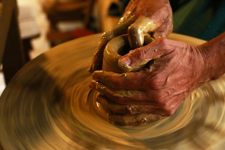 hands are molding a piece of clay on a spinning pottery board.