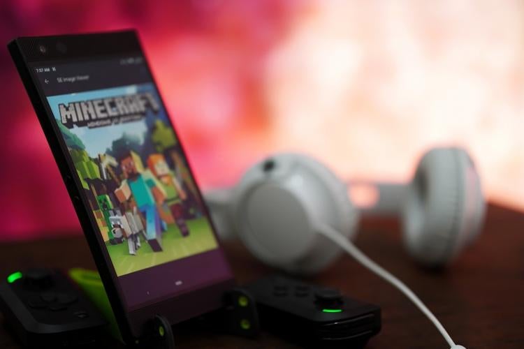 Photo illustration courtesy of Amrothman, Pixabay.com a phone screen shows characters from a videogame with headphones beside it and a soft red illuminated background