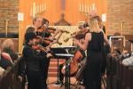 Performers stand playing string instruments in a church