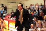 Coach Cunningham is dressed in a black suit and tie, seen yelling towards off-frame players. He is standing inside a sports game in the Basketball court